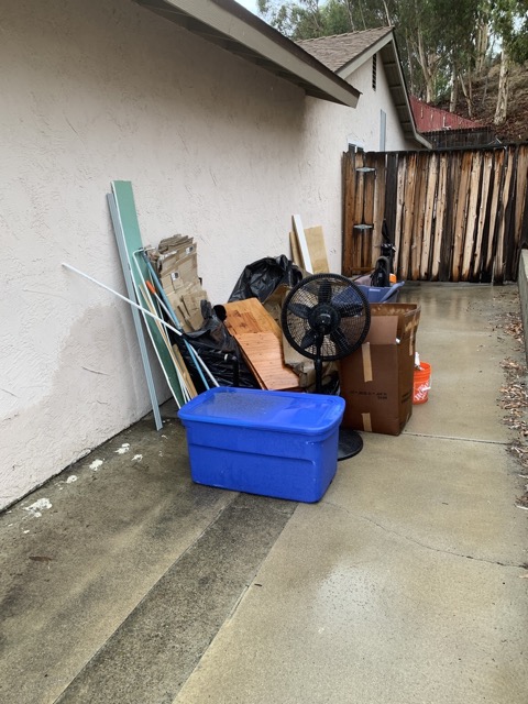 Fan, bins, and scrap piled along a side yard